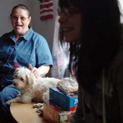 Amy Cooper, on left, laughs as she pets dog Max and listens to her "granddaughter" Jazmine Stevens, talk in the living room of their Bangor home on Monday. Although she is not biologically related to the teen, Cooper, age 65, has been raising Jazmine and her younger borther Chris since they were infants due to their birth mother's inability to care for them. Seeing a need for emotional and financial support among guardians in similar situations, Cooper is active in Maine Kids-Kin, a program of Families and Children Together, and often organizes fundraisers for the group.