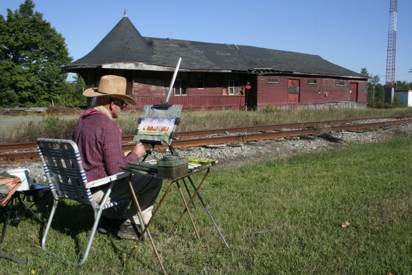 The artist Milt Christianson paints the Greenville Junction Depot. Christianson designed the logo for the depot as well. The artist Milt Christianson paints the Greenville Junction Depot. Christianson designed the logo for the depot as well.