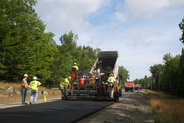 Asphalt heated to about 285 degrees is poured from a truck into a paver machine to lay a base of new road for Route 15 in Taunton & Raynham Academy Grant, near Rockwood. Watching operations are Pike Industries Paving Supervisor Rod Faloon (from left) and Maine Department of Transportation Quality Assurance Supervisor Dee Giggey. Asphalt heated to about 285 degrees is poured from a truck into a paver machine to lay a base of new road for Route 15 in Taunton & Raynham Academy Grant, near Rockwood. Watching operations are Pike Industries Paving Supervisor Rod Faloon (from left) and Maine Department of Transportation Quality Assurance Supervisor Dee Giggey.