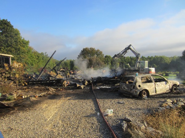 An excavator digs out potential hot spots after the metal roof of a post-and-beam barn fell onto a concrete floor. An excavator digs out potential hot spots after the metal roof of a post-and-beam barn fell onto a concrete floor.