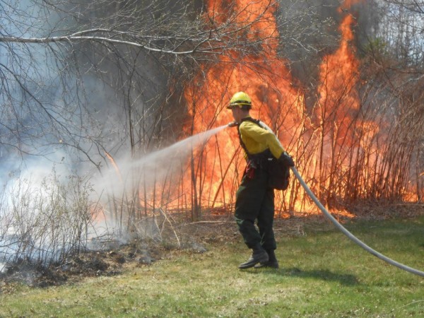 A Maine Forest Ranger uses a fire hose to douse a fire with high flame lengths earlier this year. He is wearing all of the protective gear issued to a Maine Forest Ranger, including Nomex fire-resistant pants and shirt, leather boots and gloves, a hard hat, eye protection, a portable radio and a backpack containing a fire shelter. A Maine Forest Ranger uses a fire hose to douse a fire with high flame lengths earlier this year. He is wearing all of the protective gear issued to a Maine Forest Ranger, including Nomex fire-resistant pants and shirt, leather boots and gloves, a hard hat, eye protection, a portable radio and a backpack containing a fire shelter.