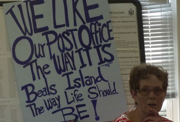 A sign next to Shirley Beal expresses the view held by islanders who showed up at the town office to meet with a Postal Service official Monday. The Postal Service is considering reducing the hours of the town's post office, where all residents have to pick up their mail. A sign next to Shirley Beal expresses the view held by islanders who showed up at the town office to meet with a Postal Service official Monday. The Postal Service is considering reducing the hours of the town's post office, where all residents have to pick up their mail.